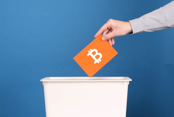 A person dropping an orange envelope with a white bitcoin symbol into a ballot box